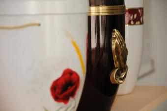 Nahaufnahme eriner weißen Urne mit einer roten Rose und einer schwarzen Urne mit betenden Händen