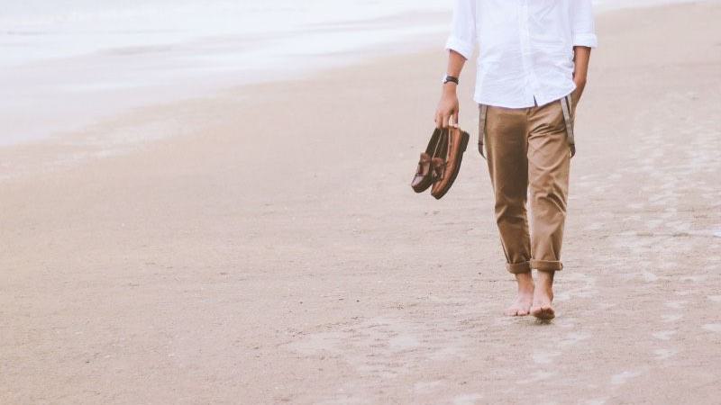 ein Mann geht barfuß am Strand mit seinen Schuhen in der Hand